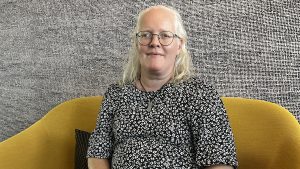 Ett foto av Linda Eriksson. Linda har glasögonen och en svartvit blus och sitter i en gul soffa.
