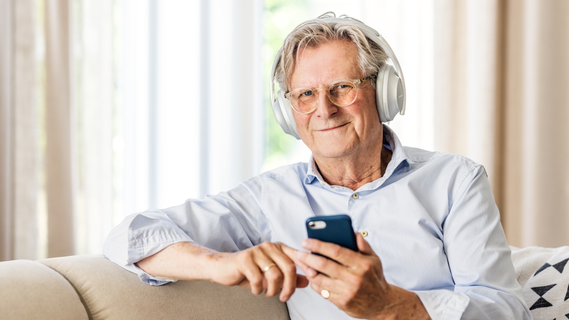 En man lyssnar på en talbok med ett par hörlurar och en mobiltelefon