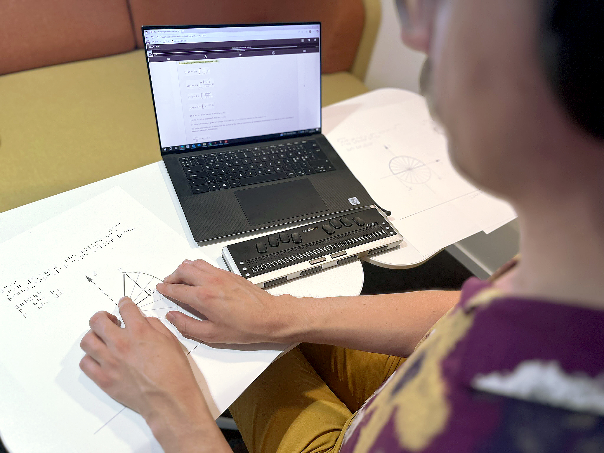 En kvinna sitter framför en bärbar dator och läser med punktskriftsläsare.
