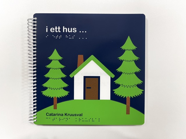 Omslaget på boken I ett hus. Illustration med en vit liten stuga omgiven av två gröna granar.