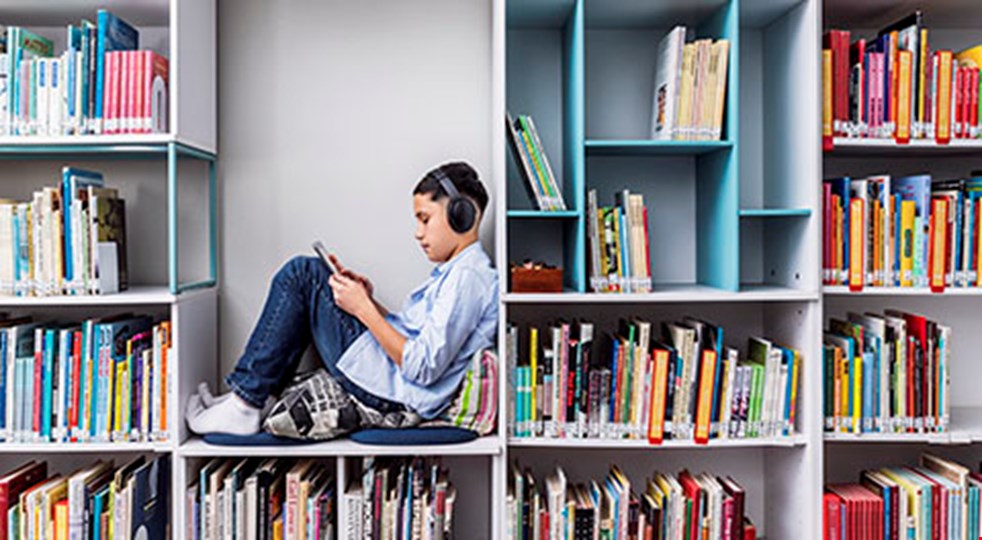 En pojke sitter och läser i en stor hylla. Runt omkring honom finns hyllor fyllda med böcker.