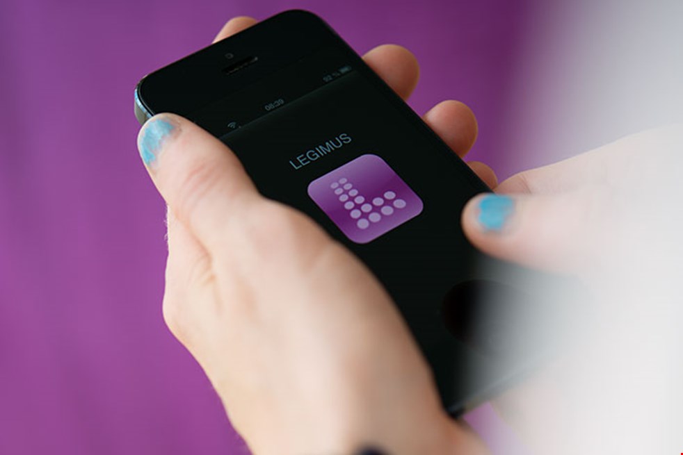 Bild på en tjejs händer med ljusblå nagellack som håller en mobiltelefon med Legimus logotyp på.