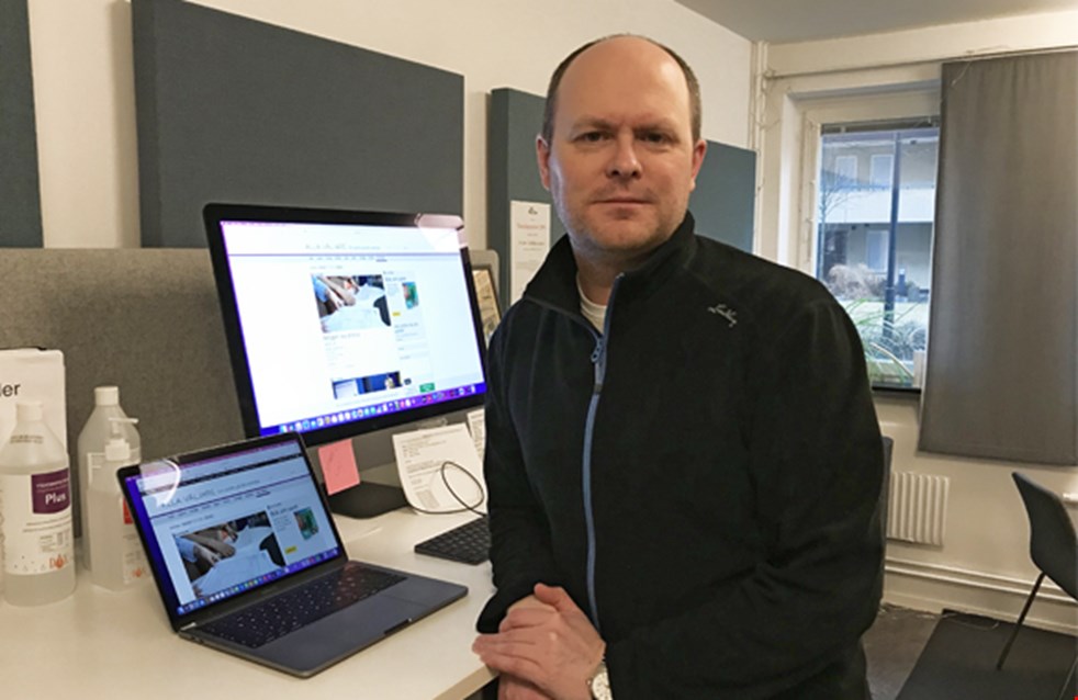 Martin Hanberg står vid ett skrivbord med två skärmar och en laptop. På skärmarna visas webbsidorna Alla väljare och 8 Sidor. 