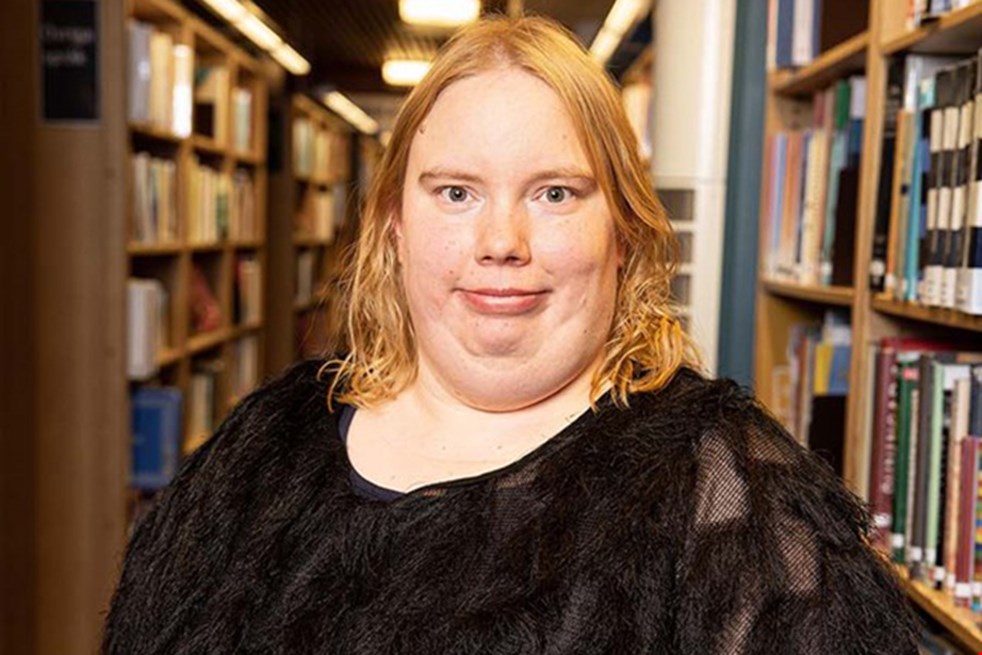 Maila Goman, Årets läsombud 2022, står i svarta kläder framför en bokhylla.