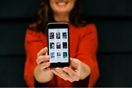En kvinna med röd tröja håller fram en mobiltelefon som visar nio e-böcker.