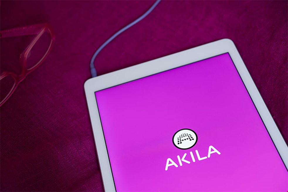 Bilden visar en läsplatta som ligger på en bord med lila duk. På skärmen syns Akilas logga på en lila bakgrund. 