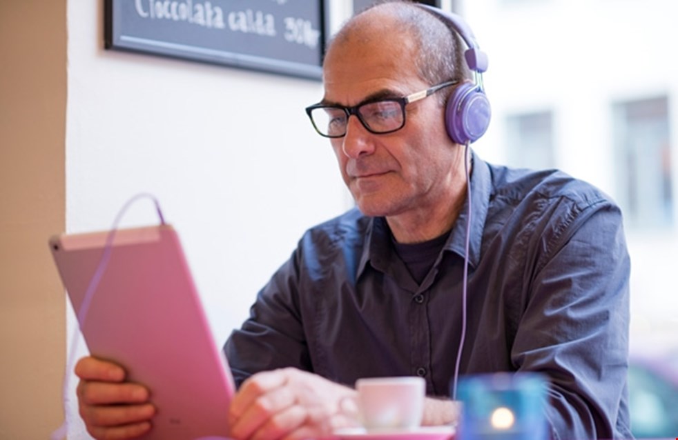 En man med hörlurar läser en talbok på en Ipad.