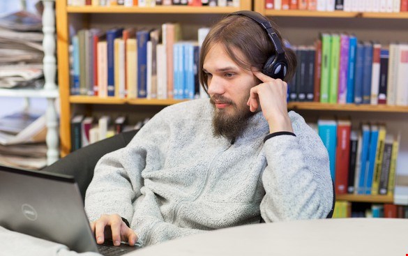 En ung man tittar på sin dator och lyssnar med hörlurar