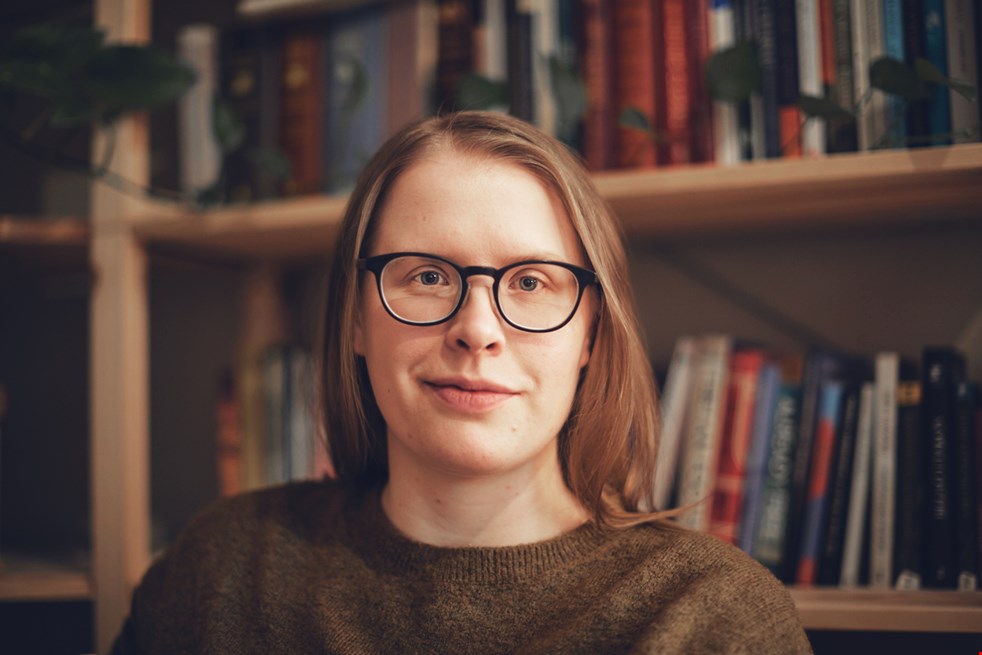 Ett porträtt av en kvinna med glasögonen som har en stor bokhylla bakom sig.