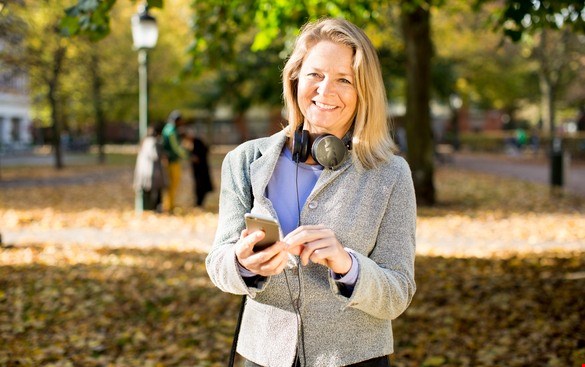 En kvinna med mobiltelefon i handen och hörlurar