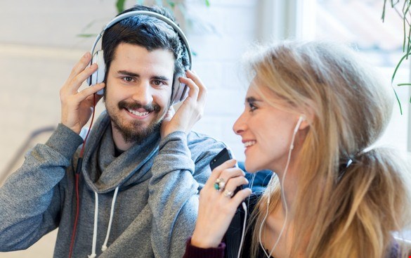 En ung man och en ung kvinna skrattar och lyssnar pånågot via hörlurar som de har på sig