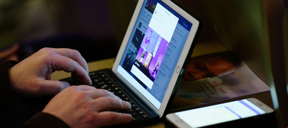 Bilden visar ett par händer som knappar på en dator vid ett webbinarium. Bredvid ligger en mobiltelefon.