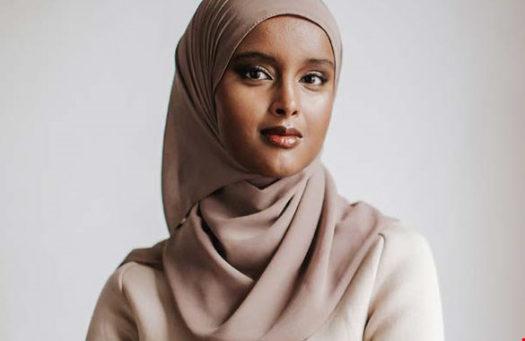 Bilden visar en porträttbild av Suad Ali i en beige hijab framför en grå vägg.